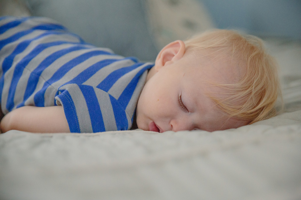 baby boy in blue onesie sleeping on his parents bed 