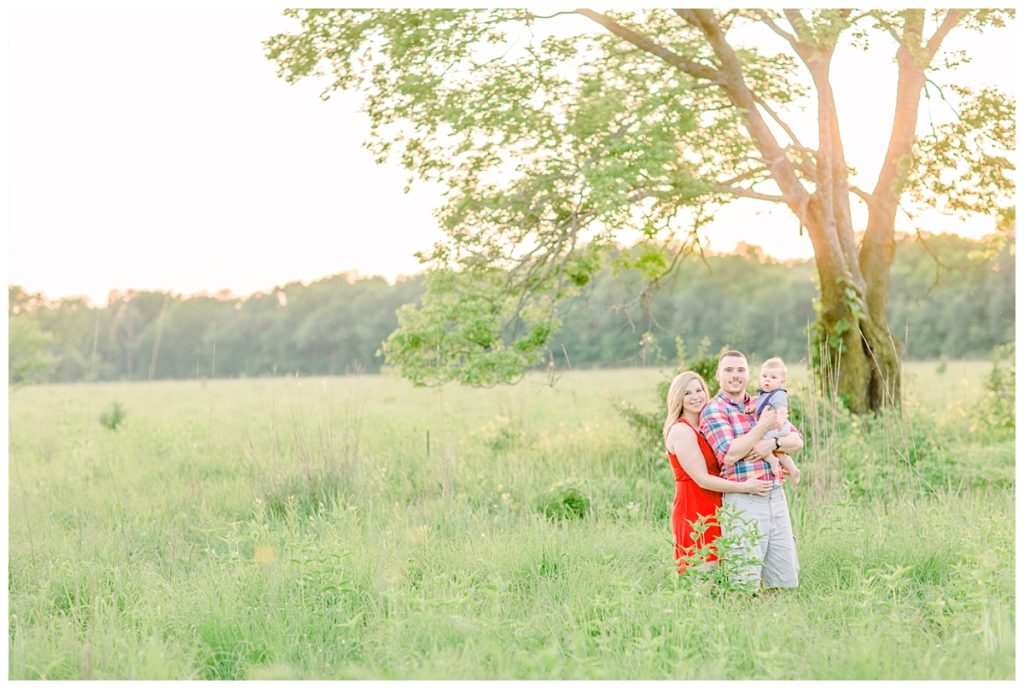 Eau Claire Family photos image taken in an open field Mom wears a red dress, Dad matches in a dress shirt holding baby