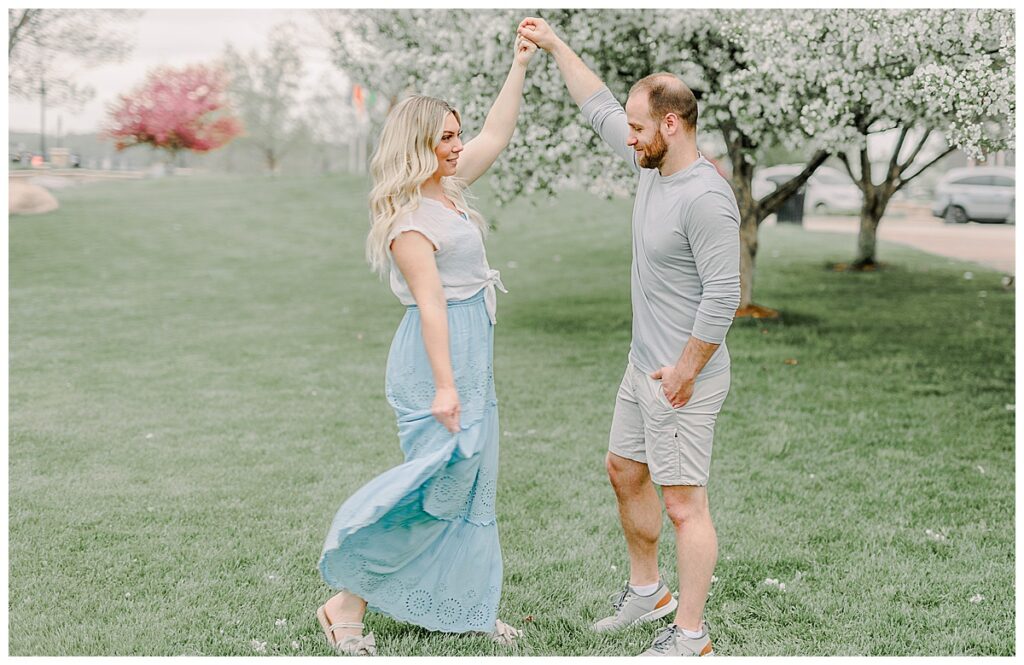 Husband twirling his wife at Phoenix Park in Eau Claire, Wisconsin with blossoms in the background of the photo