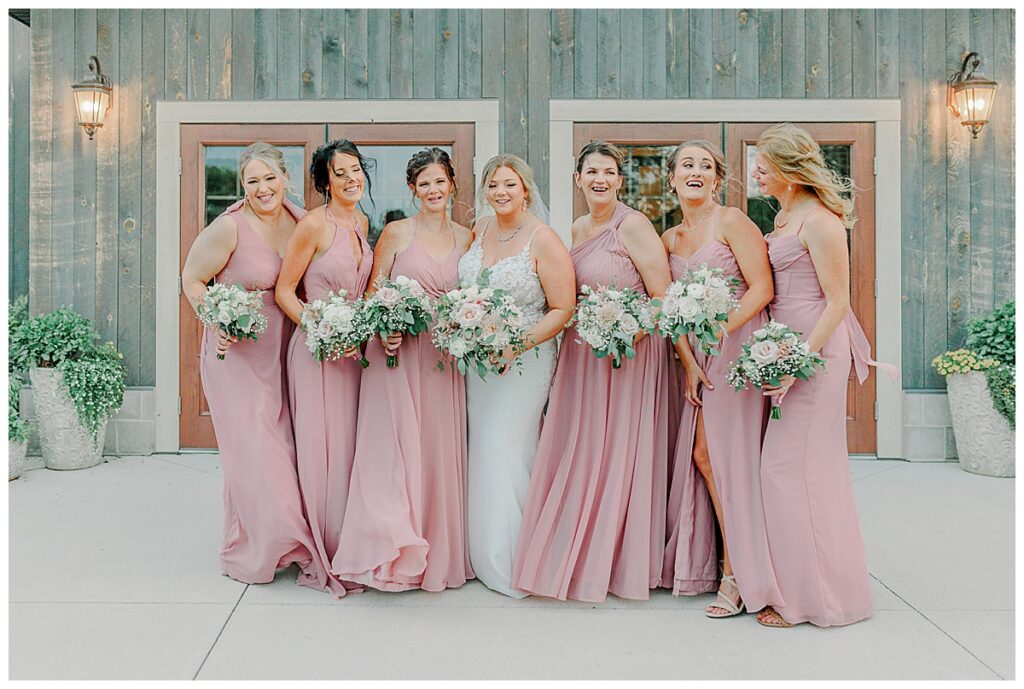 wedding bridesmaids laugh at one another wearing flowy pink dresses at lillydale dance hall in Chippewa falls Wisconsin