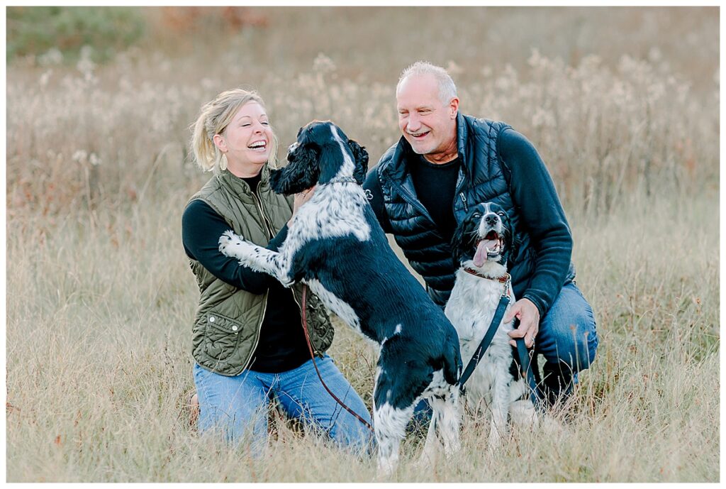 married couple and their 2 dogs posing in a field during family photography session in EAU CLAIRE, Wisconsin Photo taken by Alisha Marie Photography specializes in family photos in Eau Claire, Eau Claire Family photos. Eau Claire Family Photographer