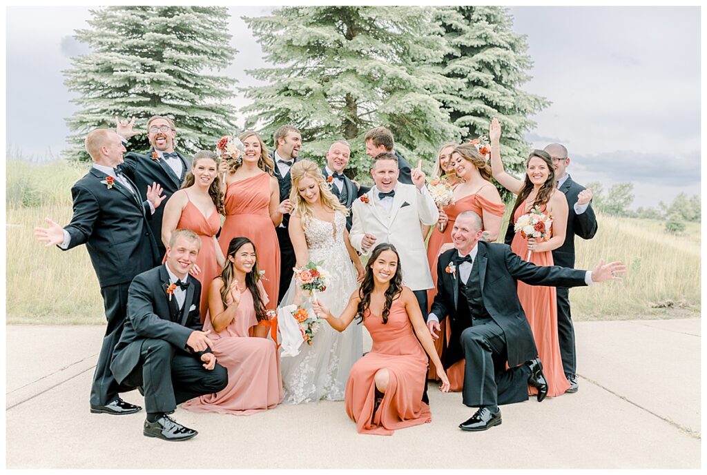 bride and groom dancing with wedding party, posed in coral color dresses, holding summer wedding bouquets at a Minnesota wedding venue