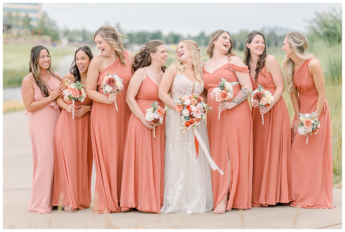bride laughing with bridesmaids, posed in coral color dresses, holding summer wedding bouquets at a Minnesota wedding venue