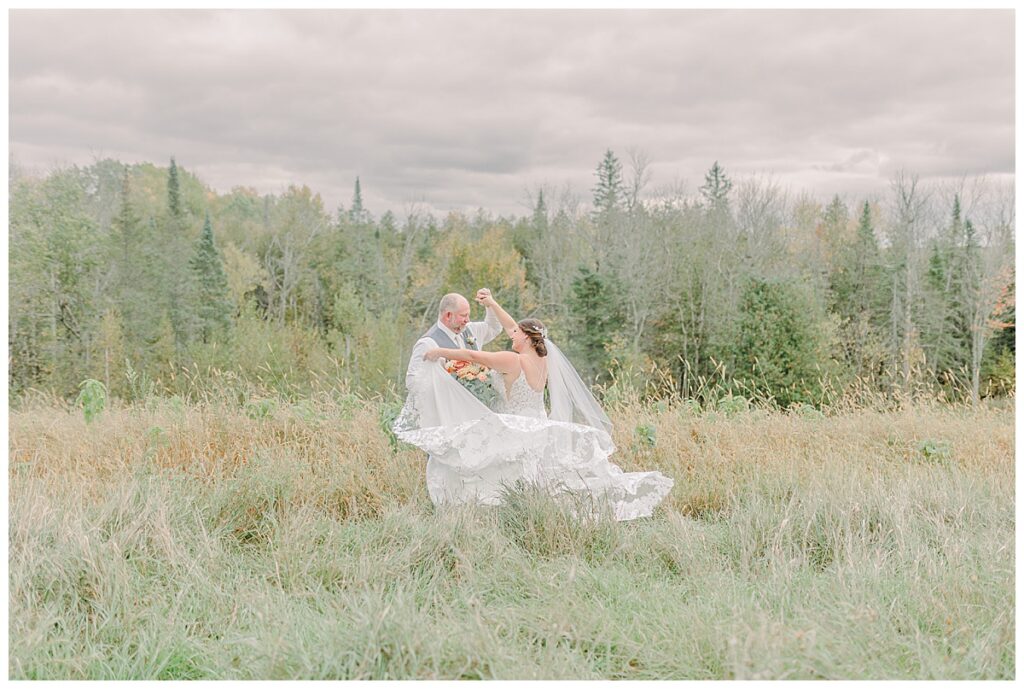 A bride and groom stand in a field and the bridle twirls, showing off her beautiful wedding dress and long train. Image by Alisha Marie Photography at the wedding venue alluring acres not far from Minneapolis, Minnesota and St. Paul