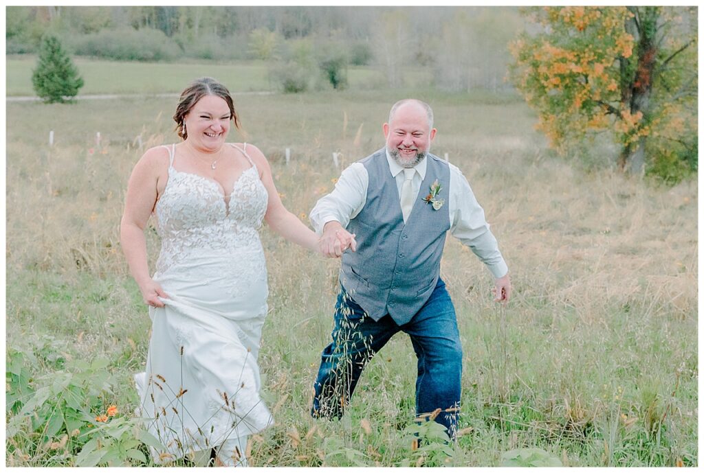 Bride and Groom hold hands, laugh and run in a field. captured by Alisha Marie Photography at the wedding venue alluring acres near Chippewa Falls Wisconsin