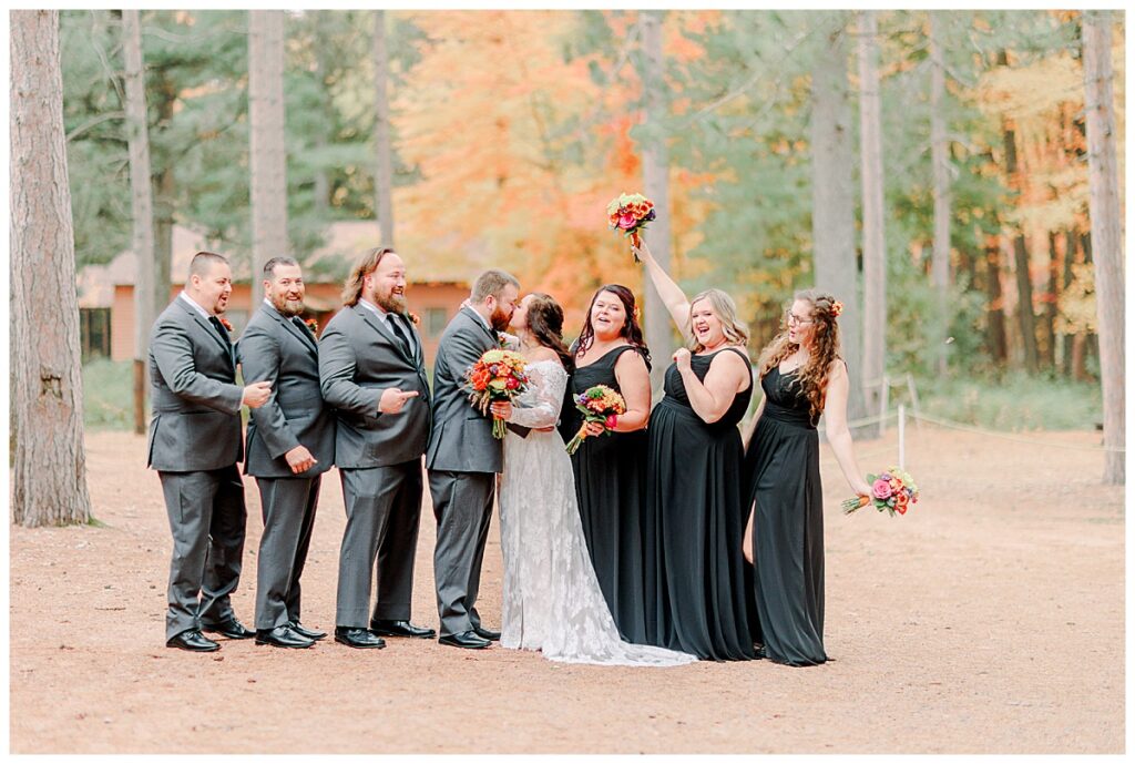 Wedding party laughing outside wisconsin wedding venue Lake Wissota Fall wedding photography taken by Alisha Marie Photography wedding day, bride with her bridesmaids dress in black gowns